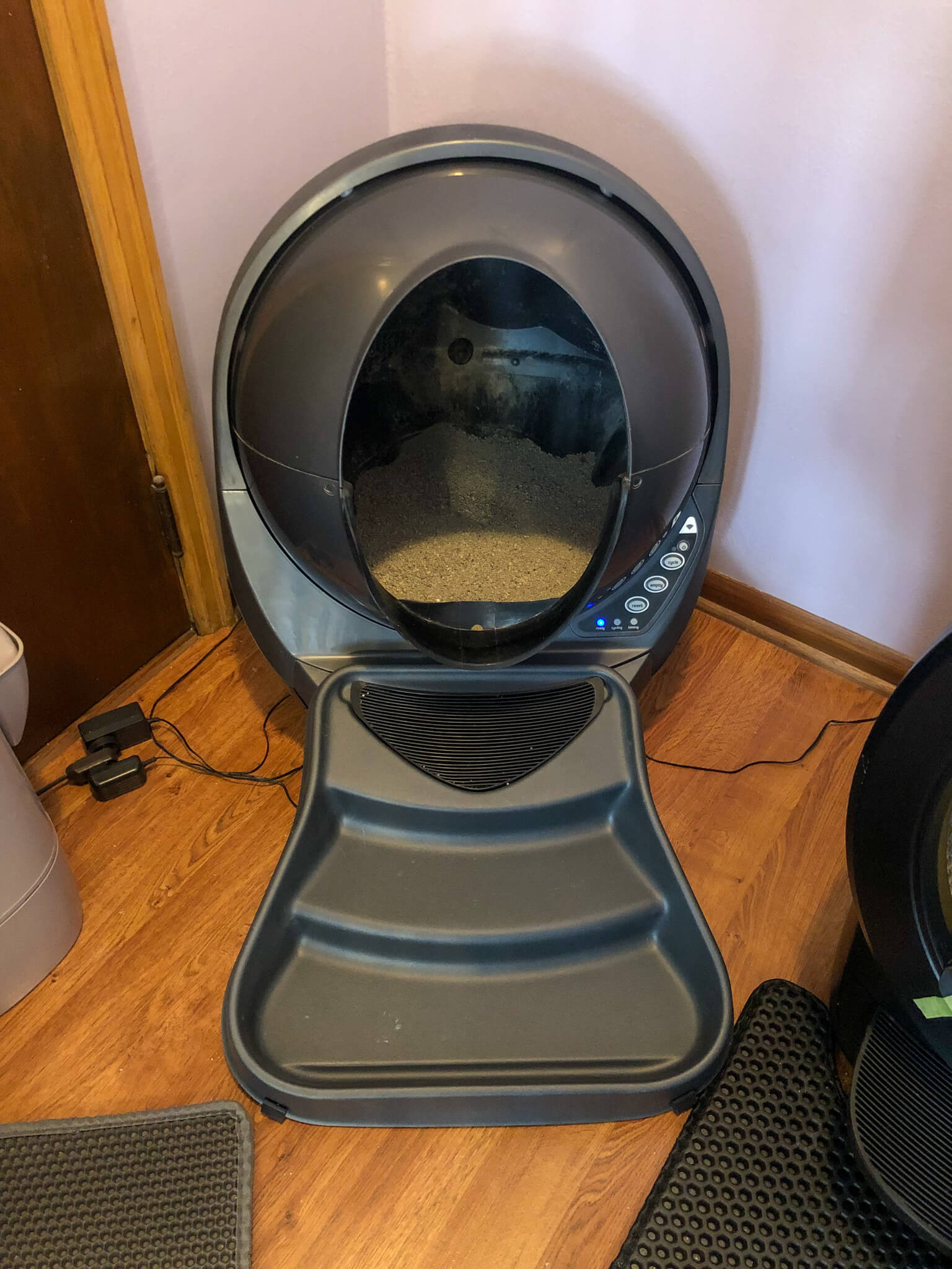 Litter Robot Connect 3 litter box with ramp for cat to walk up into it in a corner of a room.